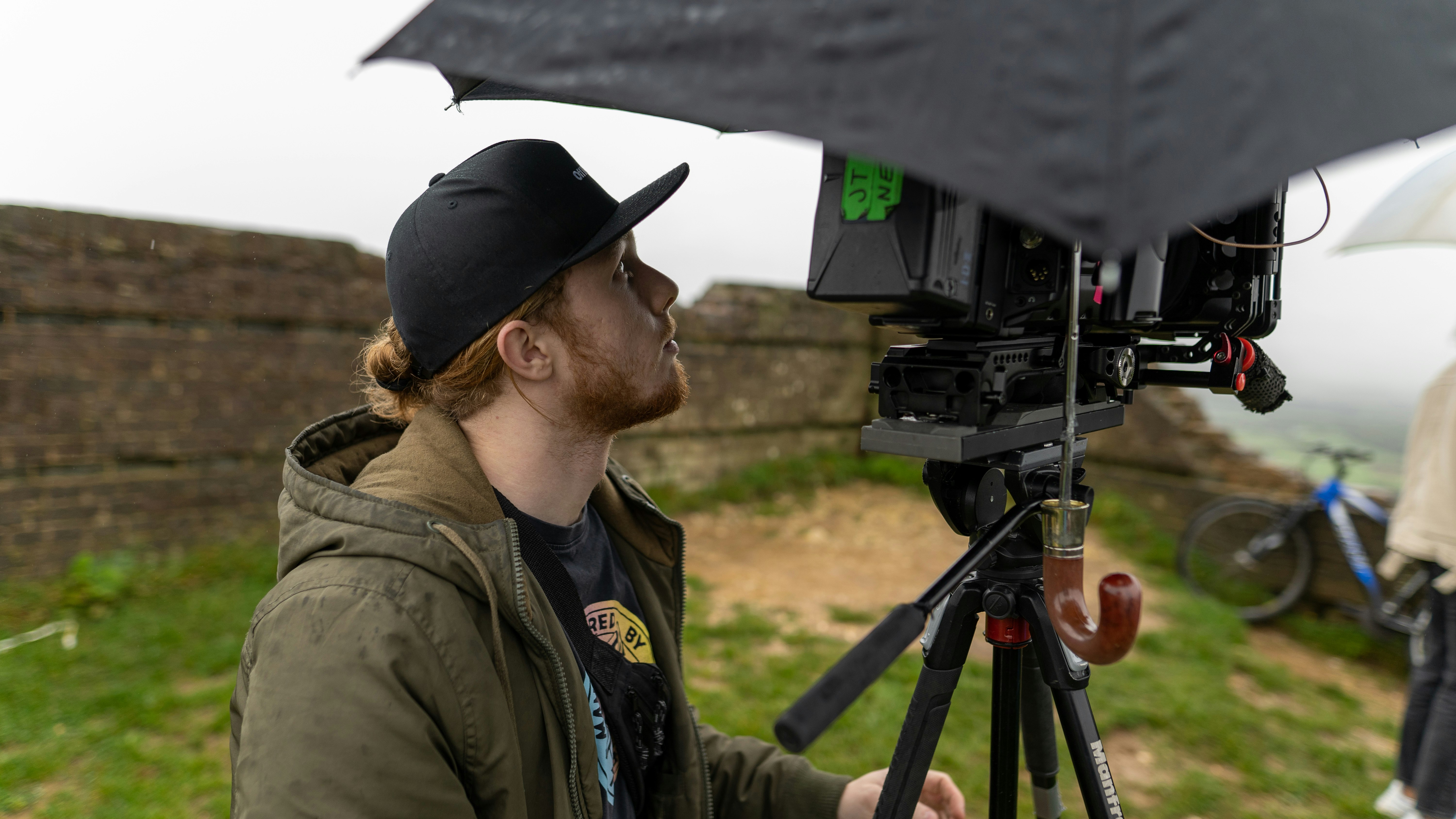 man in black cap and brown jacket looking at black camera